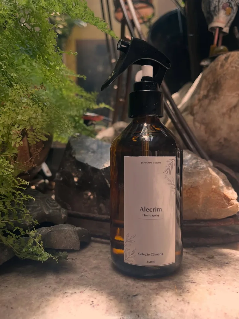 Frasco âmbar de home spray com rótulo Alecrim, entre pedras e folhagem