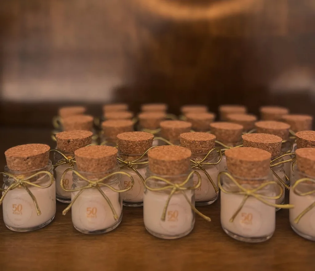 Fileiras de potinhos de vela com rolha e laço dourado, lembrança de uma festa de 50 anos