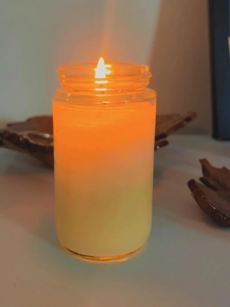 Vela acesa em pote de vidro alto, com luz quente
